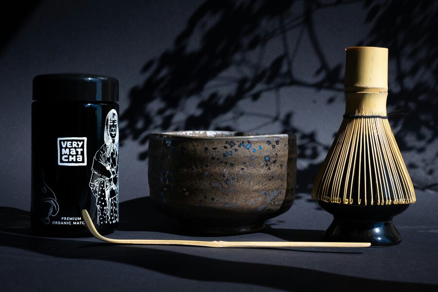 A bamboo chasen whisk preparing matcha in a black ceramic chawan bowl