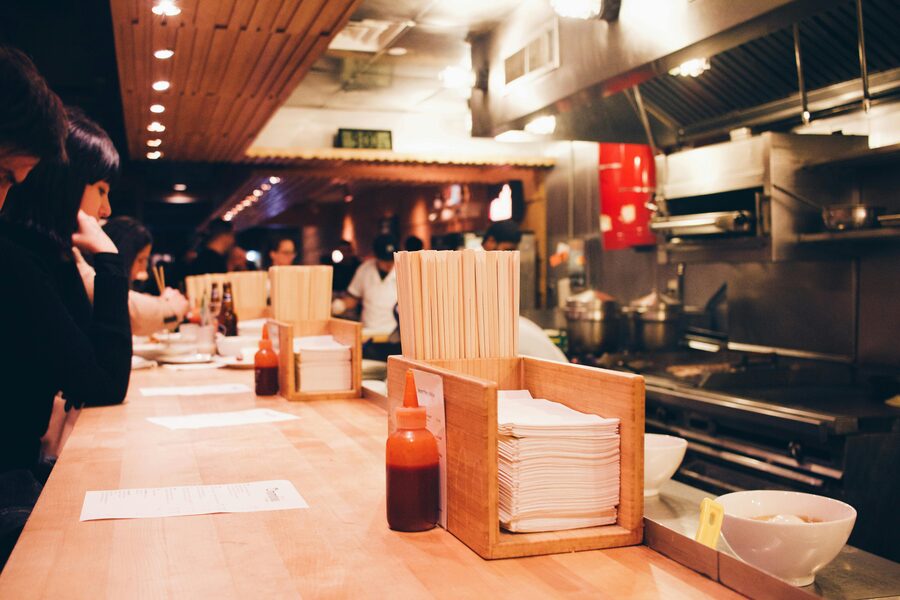 The counter of a small traditional Japanese ramen shop with stools facing the kitchen